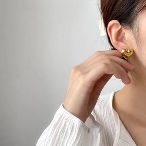 Close-up of heart-shaped gold stud earring with a glossy mirror finish on female model