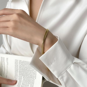 Close-up of a wide flat gold snake chain bracelet on a woman wrist in a luxury setting