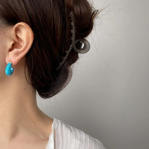 Détail d'une boucle d'oreille spirale bleue texturée portée par un mannequin sous une lumière douce