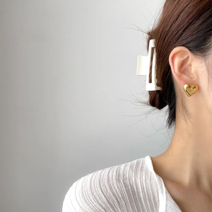 Detail of a golden heart stud earring and a white geometric hair clip on a female model