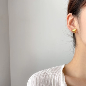 Detailed view of matte gold triangle earrings worn for modern geometric style