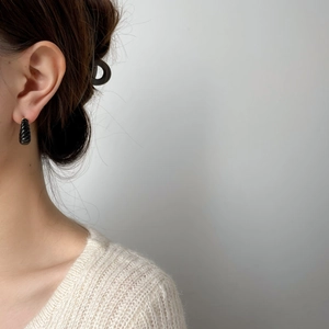 Détail d'une boucle d'oreille demi-créole noire striée sur l'oreille au style épuré
