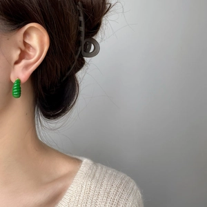 Gros plan sur un mannequin portant des boucles d'oreilles spirales émaillées vertes