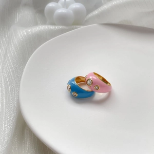 Détail de bagues en émail bleu et rose avec trois zircons brillants sur soie blanche
