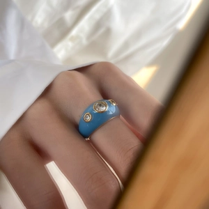Détail d'une bague en émail bleu avec bordure dorée et trois pierres en zircone cubique