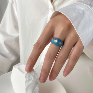 Détail d'une bague large en émail bleu ornée de zircons sur une monture dorée