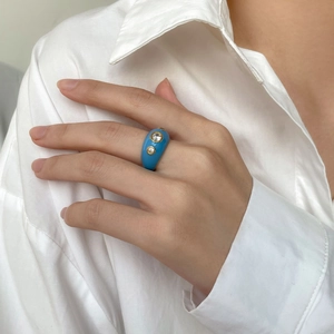 Bague large en émail bleu avec des accents de zircone en finition dorée portée à la main
