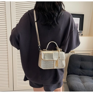 Detail of gold woven texture handbag worn by model showing compact size and metallic handle