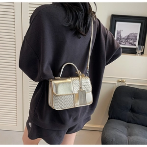 Detail of golden metallic leather crossbody bag with woven texture and metal handle
