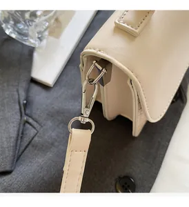 Detailed macro of silver metal buckle and woven leather texture on cream crossbody bag