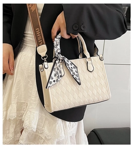 Close-up of beige quilted tote bag featuring heart pattern scarf and brand strap