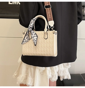 Close-up of quilted cream tote bag featuring heart scarf and logo webbing strap