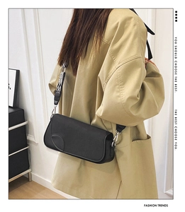 Detail of black minimalist shoulder bag featuring a geometric woven wide strap on trench coat