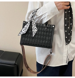 Detail of black quilted tote bag featuring white stitching and printed ribbon strap
