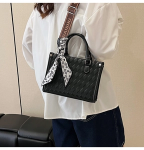 Detail of black quilted tote bag with decorative heart scarf and letter strap