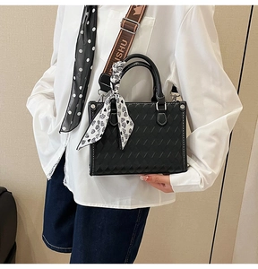 Detail of black quilted tote bag featuring a heart pattern scarf and wide shoulder strap