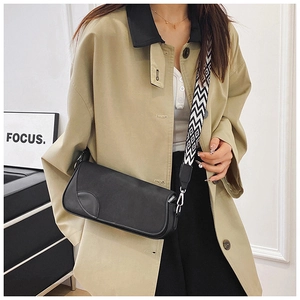 Detail of black leather crossbody bag featuring unique curved flap and geometric wide strap