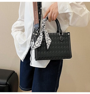 Detail of black quilted tote bag with decorative silk scarf and wide branded strap