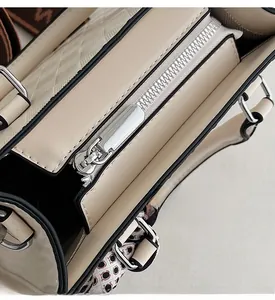 Close-up of beige quilted tote showing silver metal zipper and black edge paint details