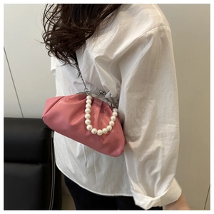 Detail of pink dumpling bag with pearl handle and metal clasp closure on white shirt