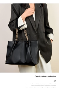 Dettaglio borsa shopper in pelle nera con catena dorata indossata da modella
