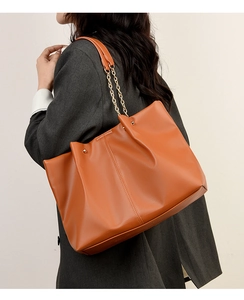 Borsa tote in pelle marrone arancio con catena indossata su un blazer grigio