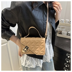 Detail of light khaki quilted crossbody bag with golden hardware and chain lock on a model