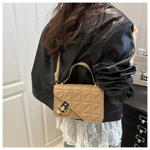 Detail of light brown quilted handbag with gold hardware styled on leather jacket
