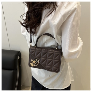Detail of dark brown quilted crossbody bag with gold lock and chain on shoulder