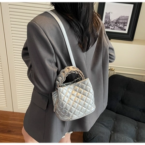 Detail of silver quilted bucket bag featuring a woven handle and metallic finish surface