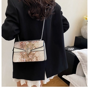 Détail du sac à chaîne à motif serpent porté avec un blazer noir et une jupe blanche