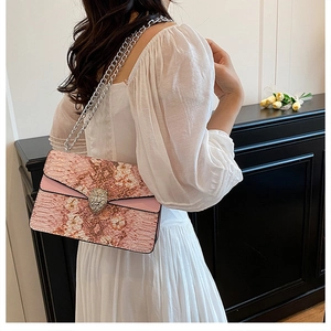 Sac bandoulière rose motif serpent avec fermoir tête d'aigle porté par un modèle