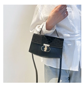 Detail of black crossbody bag with gold hardware and textured flap on model