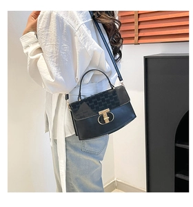 Detail of black leather handbag with embossed patterns and a golden T-shaped metal clasp