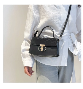 Detail of black crossbody bag with golden T-lock and embossed letter texture detail