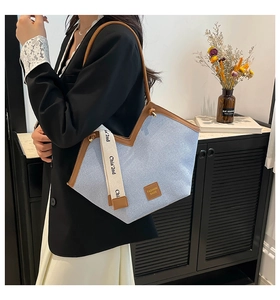Detail of light blue denim tote with brown leather trim and woven logo shoulder strap
