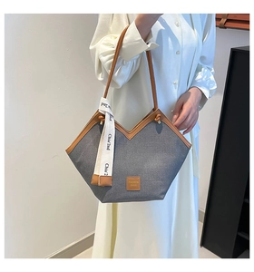 Detail of grey denim tote bag showing brown leather trim and white branded ribbon straps