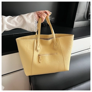 Detail of bright yellow tote bag showing pebbled leather texture and front zipper pocket