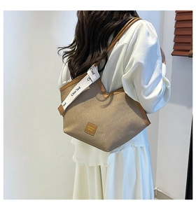 Detail of canvas tote bag with brown leather trim and branded wide webbing shoulder strap