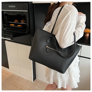 Detail of black litchi grain leather tote bag with a golden zipper outer pocket
