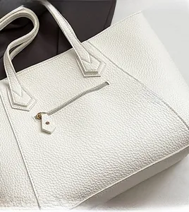 Detail of white lychee leather tote bag featuring golden zippers and textured finish