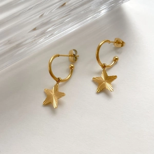 Detail of gold C-shaped hoop earrings featuring textured five-point star charms
