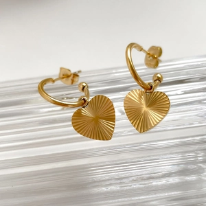 Detailed view of gold heart drop earrings with textured finish on striped glass surface
