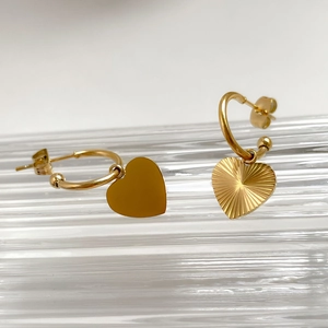Detail of asymmetric gold heart earrings with polished and pleated textures on a glass tray