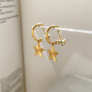 Detailed close-up of golden star drop earrings with fine sunburst texture on acrylic stand