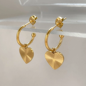 Close-up of gold heart earrings with sunburst patterns on transparent display stand