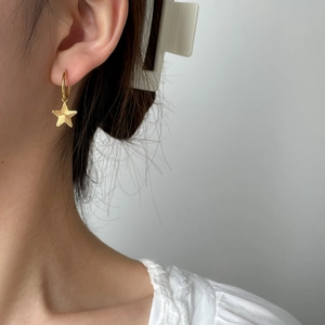 Elegant gold star pendant hoop earrings with sunburst texture worn by a model