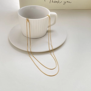 Close-up of gold double-layer snake bone necklace draped on a white coffee cup rim