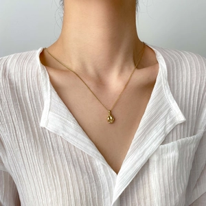 Détail du collier vintage doré avec pendentif poing sur mannequin en chemise blanche