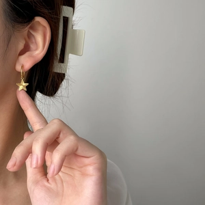 Close-up of gold star dangle earrings with textured finish worn on ear for minimalist look